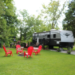 Camping setup with RV and red chairs around a fire pit